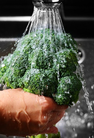 a close-up of a human hand washing broccoli in a silver sink