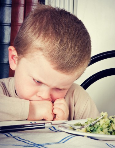 Four year old boy disliking the veggies on his plate