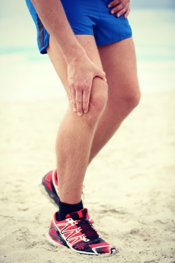 Knee pain - runner injury. Pain in knee joints in man running on beach.